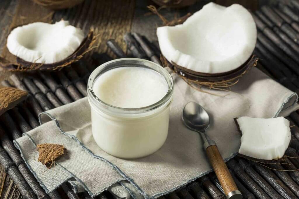 Um coco com algumas fatias de coco ao lado e também um pote de oleo de coco.